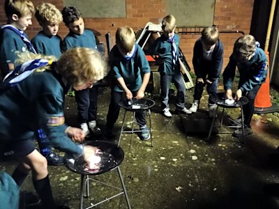 Three Cubs attempt to be the first to light their cotton wool, using a firesteel. The remaining Cubs gather around to see who will win.