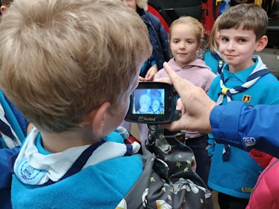 A Beaver holds a heat scanner, pointing it at the faces of two other Beavers and looking at the difference between how their faces look to their surroundings. One Beaver seems to have a cold nose.