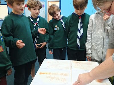 The Cubs are grouped around the table, watching the leader reveal their messages. They look really pleased with the results.