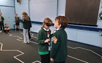 One Cub is blindfolded and making her way along a taped zigzag line, guided by the voice and instructions of her fellow Cub who has a cheeky grin on his face. In the background, we can see another pair of Cubs finishing their run of the taped line while others wait their turn.