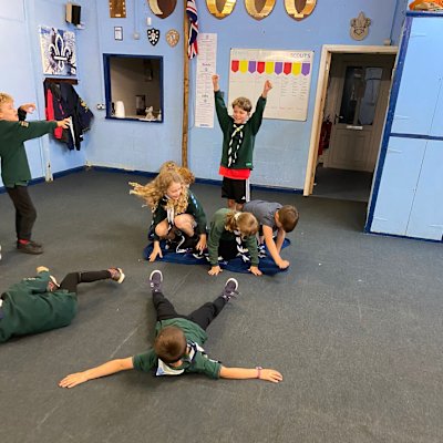 One Cub standing, arms raised in triumph with four other Cubs crouching on a blanket, two more Cubs have fallen over onto the floor while playing the magic carpet game.