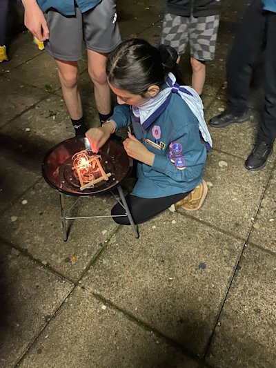 This Scout has managed to get her fire lit and is trying to keep the flame going strong enough to get the sticks burning.