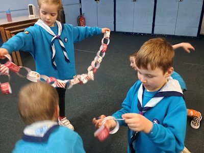 A group of Beavers are working as a team to make their paper chain longer so it can be wrapped around the Christmas tree. One Beaver is holding a swag of chain while the others work to attach their short chains together.