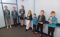 Three Scouts, two Cubs and two Beavers stand together, showing their medals and trophies.