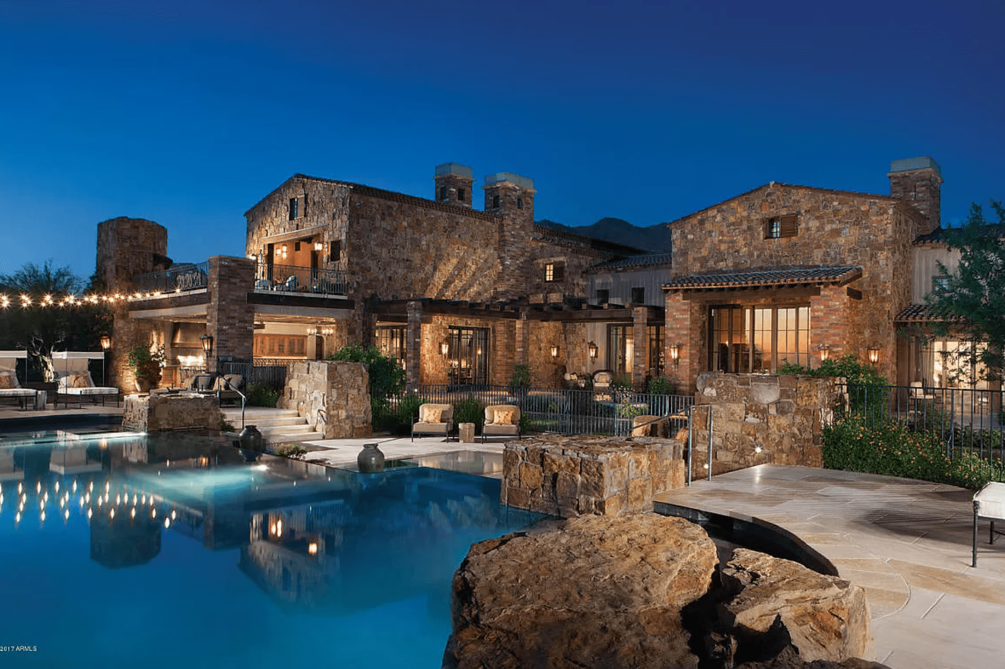 Back side view of a rock home with a pool. 
