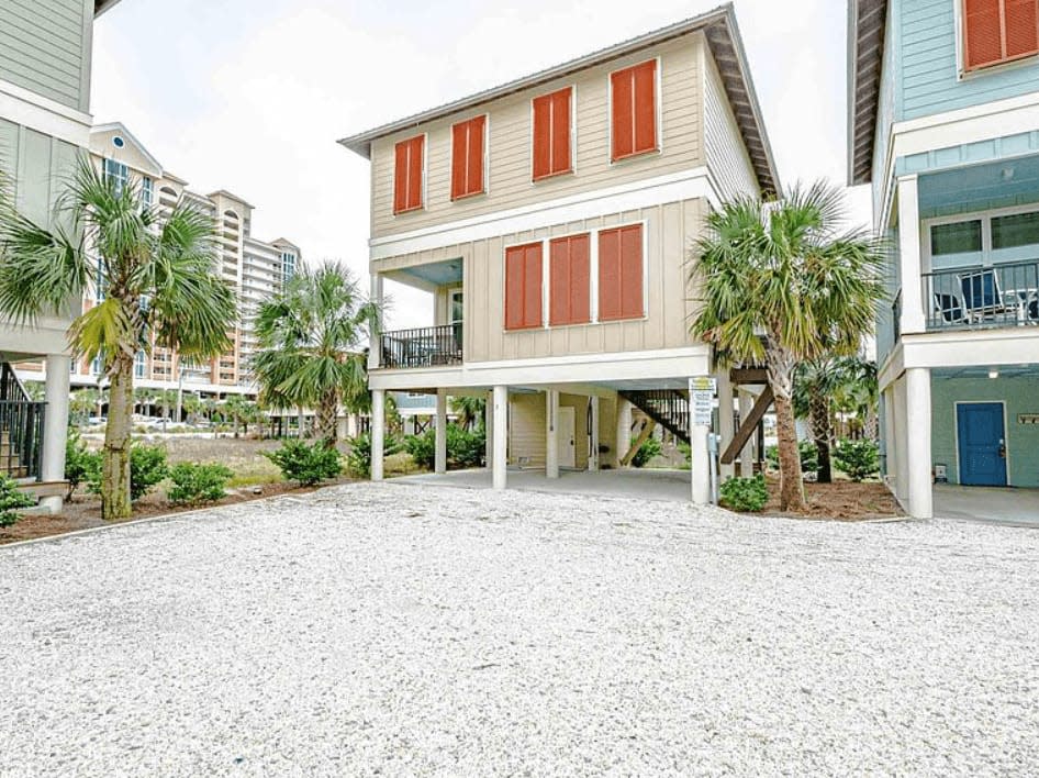 Outside view of tan beach house with orange storm shutters. 