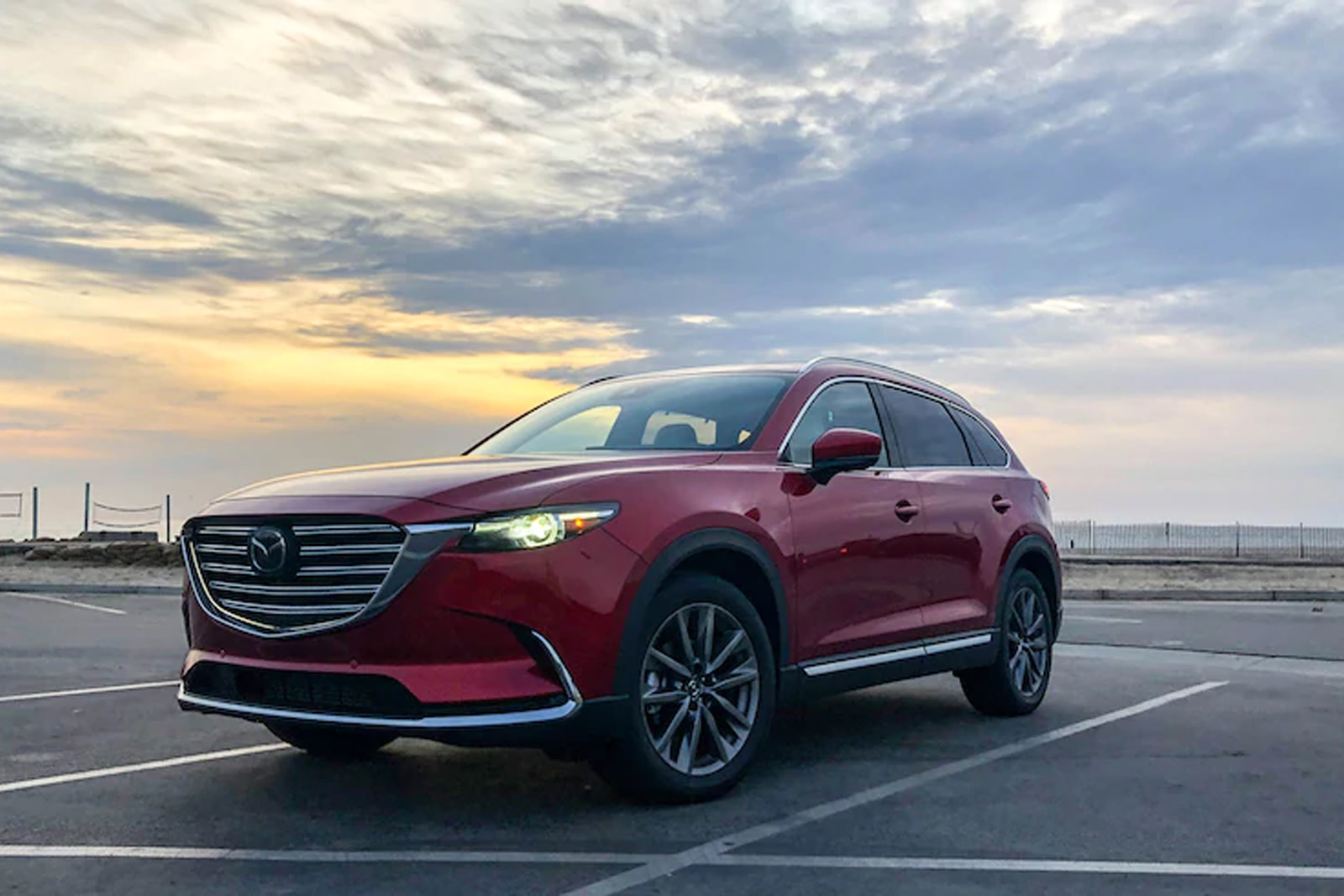 Red Mazda SUV parked in a parking spot in a vacant lot at sunset.