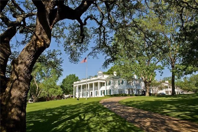 Far view of a white home with a United States of America flag flying in the front yard. 
