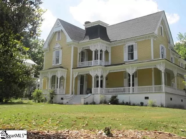 Yellow, two story Victorian style home pictured from the yard.