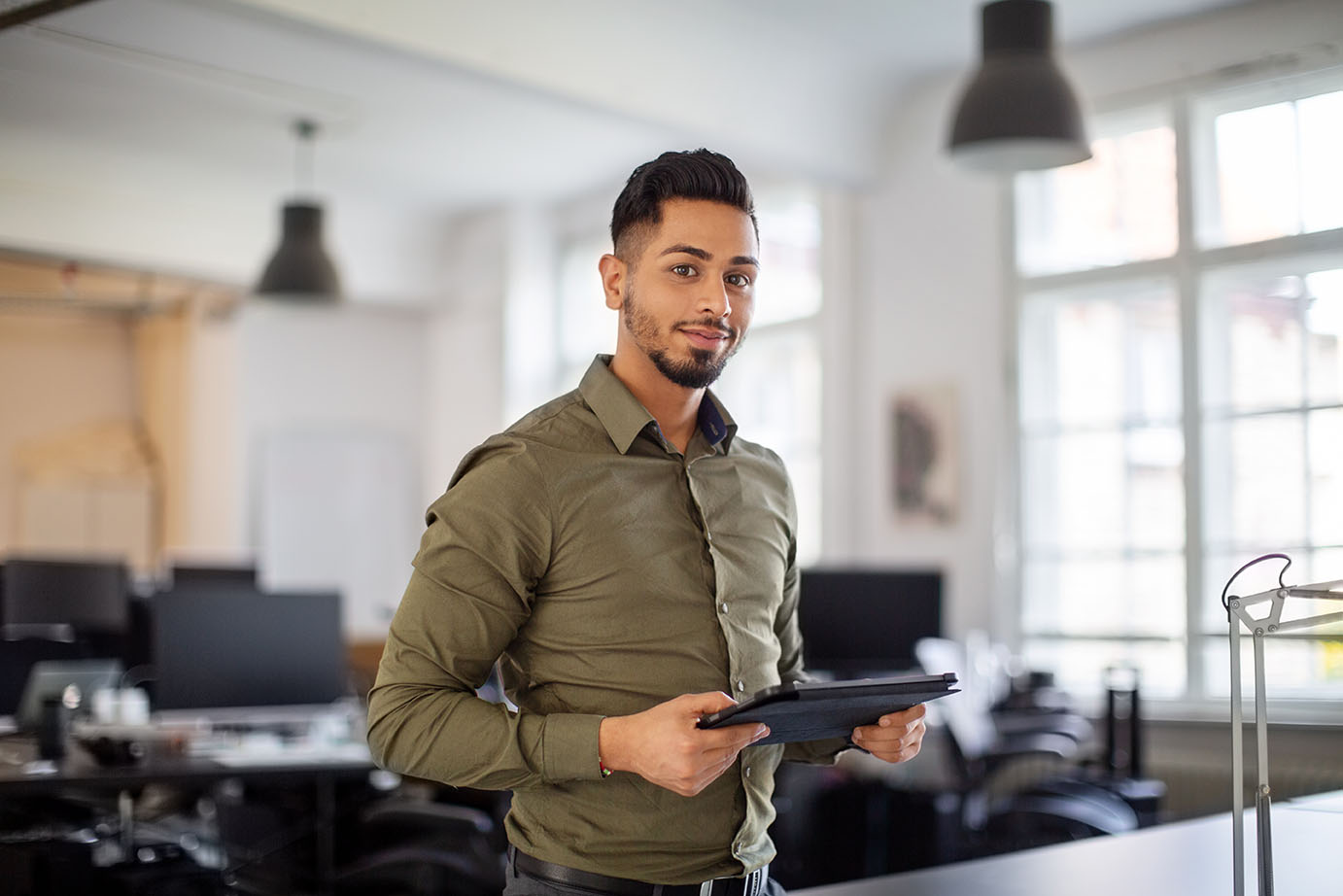 Man wearing a green button down shirt and holding a tablet in an office.