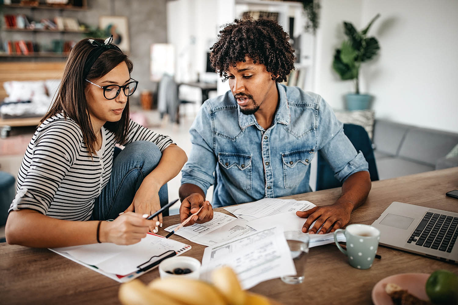 Man and woman sitting at a table looking over multiple pieces of paper and a clipboard with a page of writing.
