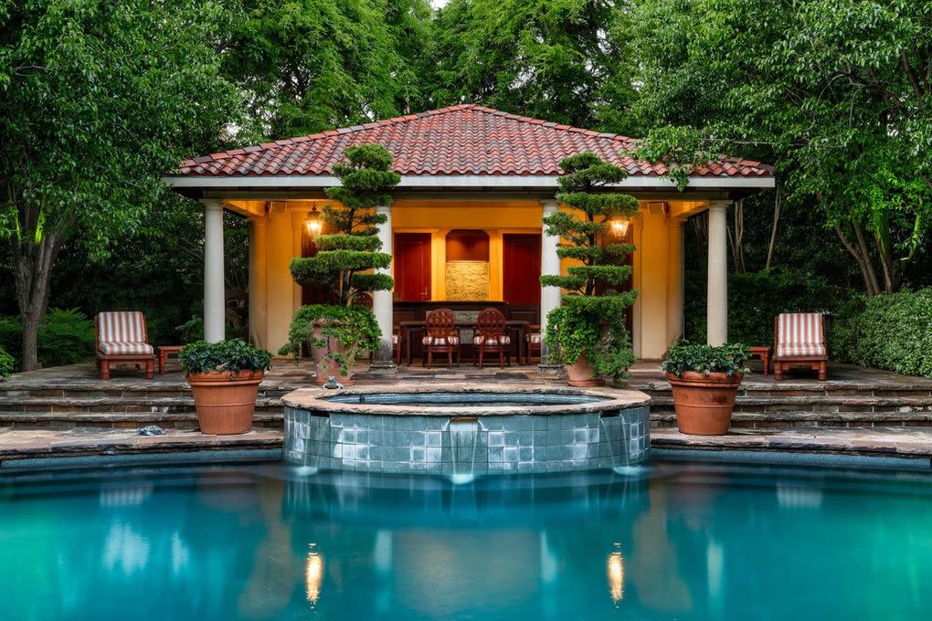 Pool side view of this orange home with two smaller trees by the entry way. 