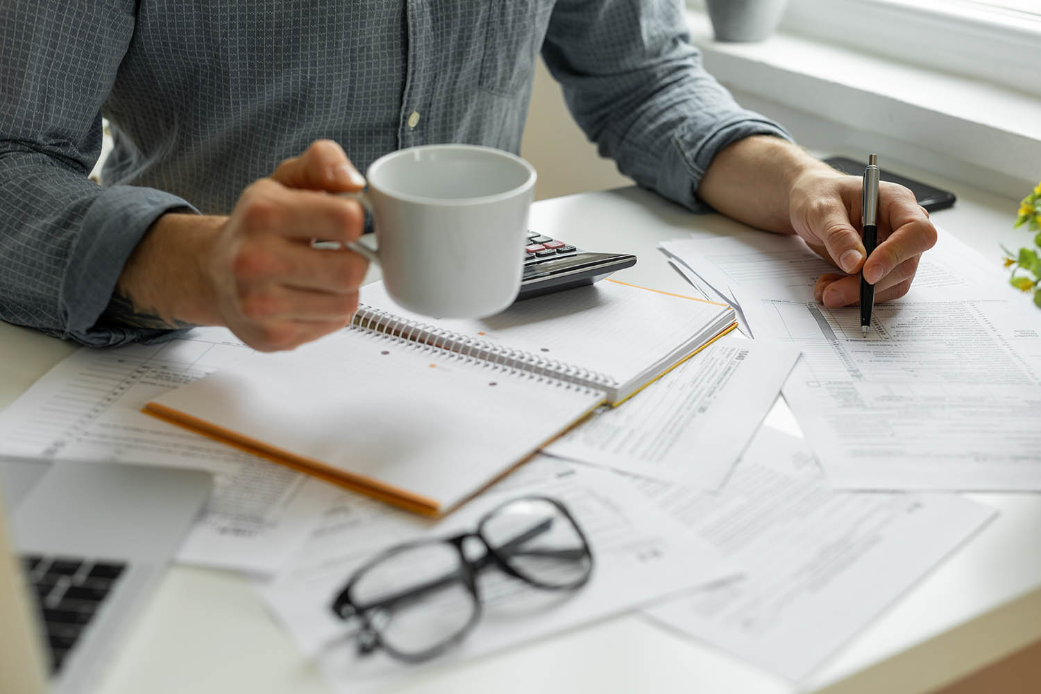 The torso of a person holding a mug and pen, and a desk with papers