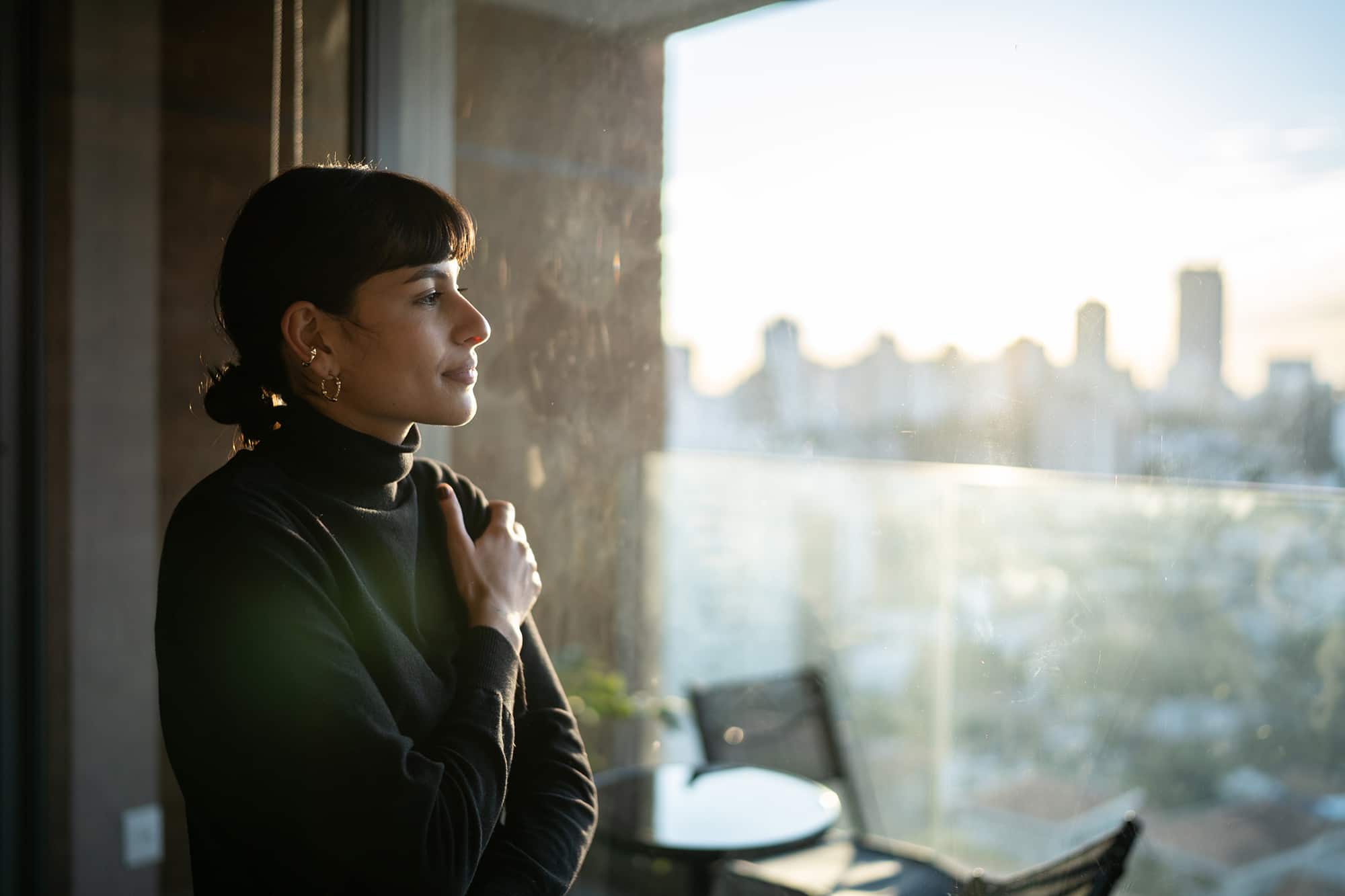 Woman with bangs and turtleneck sweater looking out a window.
