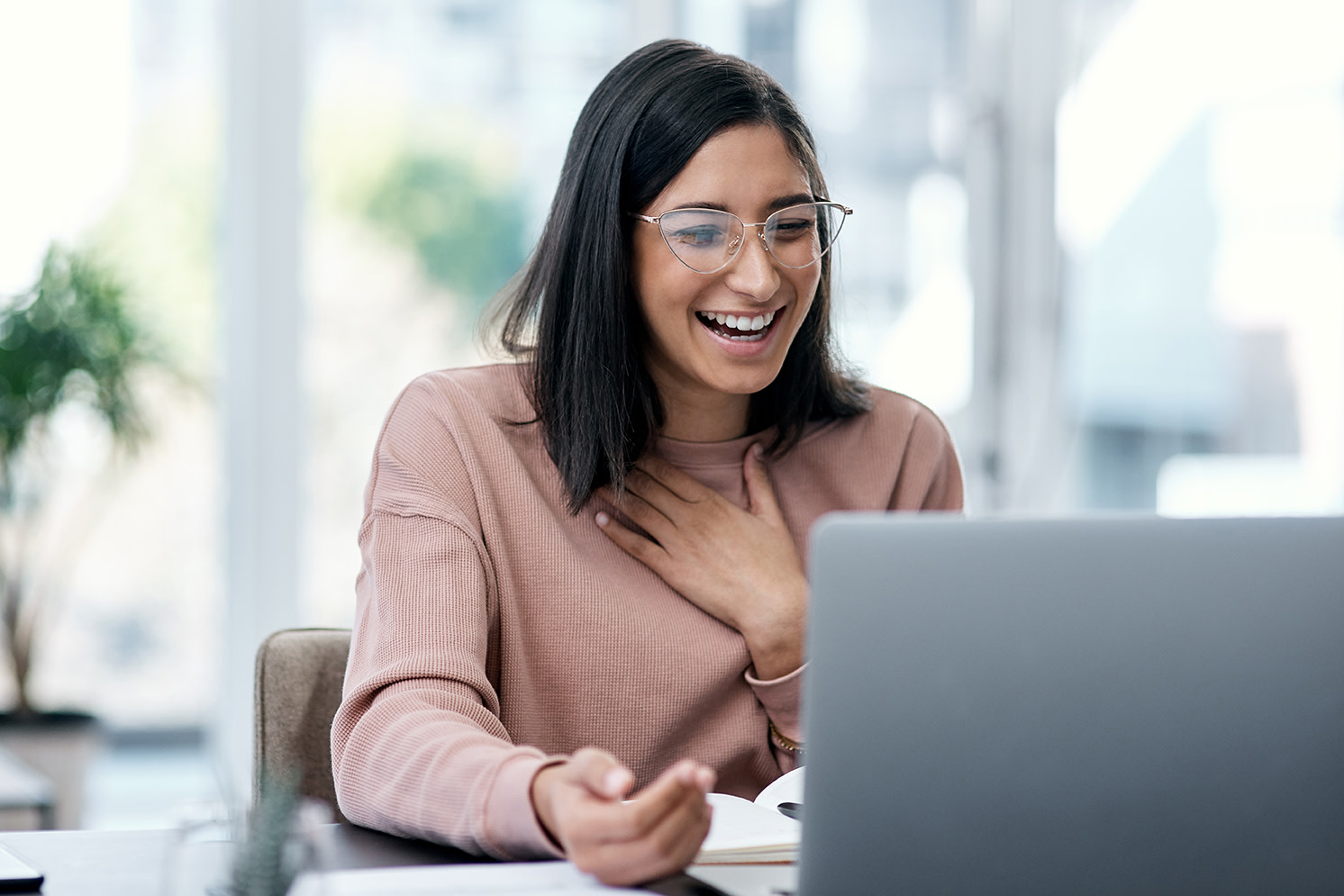 A woman sitting down laughing at her computer. 
