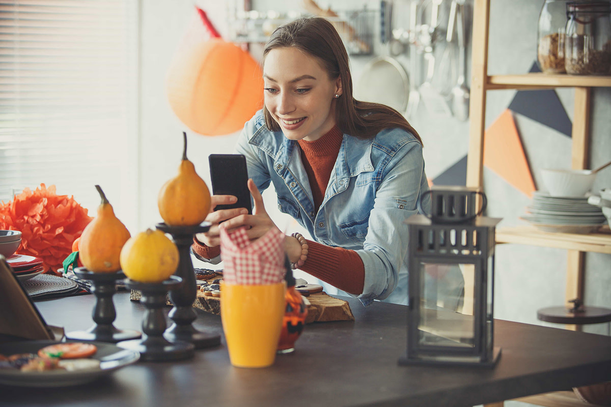 Woman smiling while taking a photo on her phone of Halloween decorations on the table.
