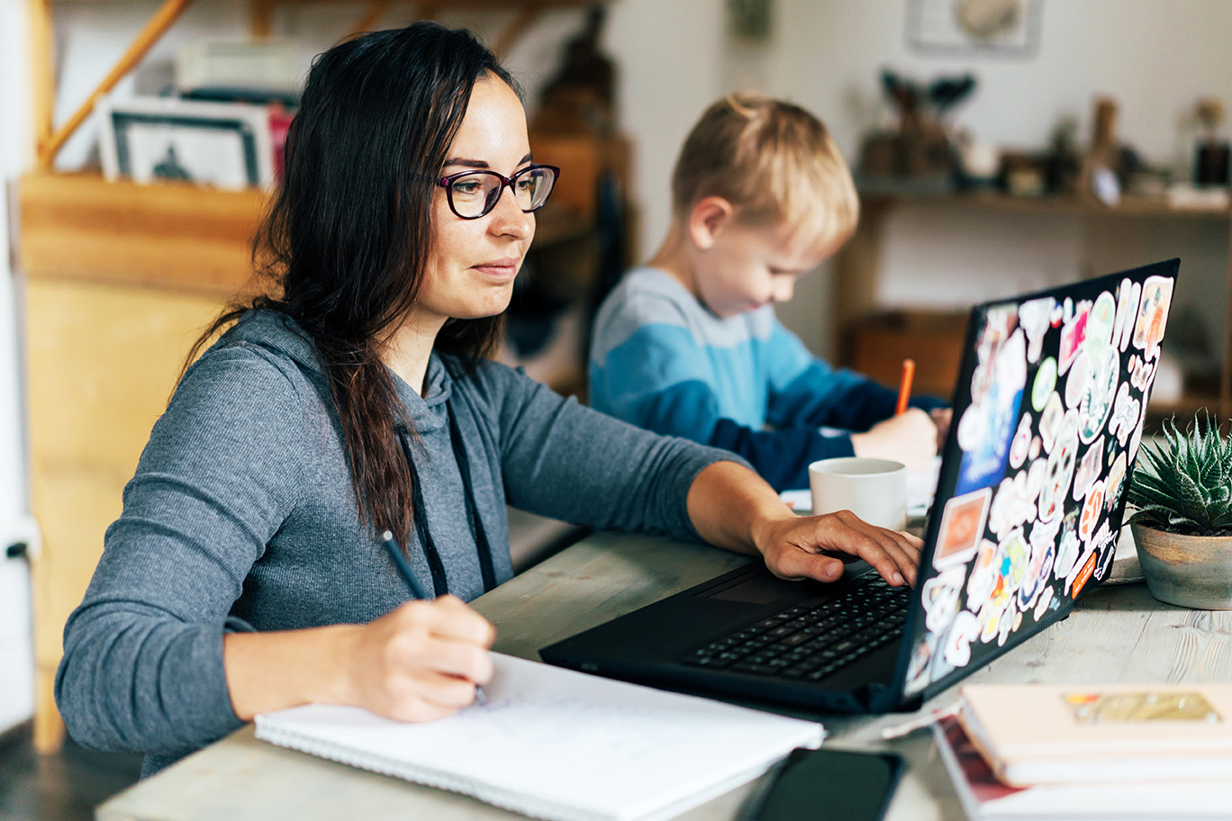 A woman on a laptop and a child sitting at a table