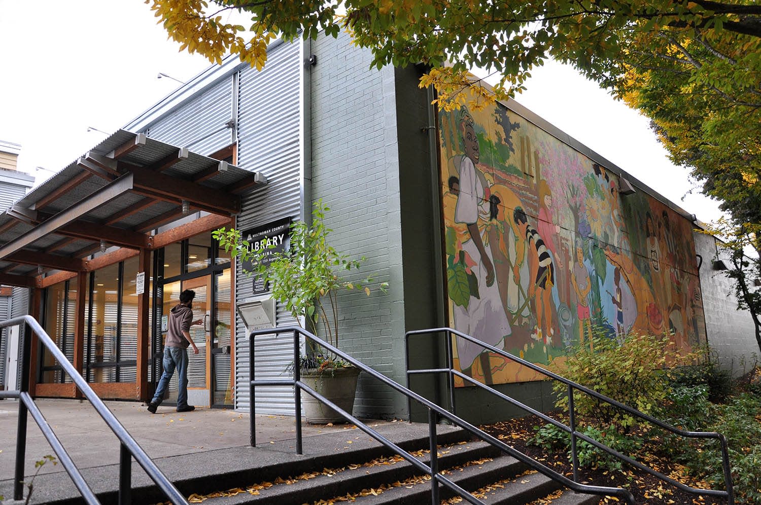 Man walking into an industrial style building with a sign that says "Library" on the front wall and a painted mural on the side wall.