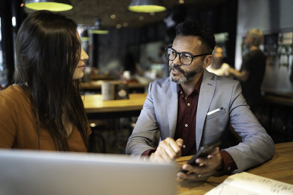 Man and woman sitting at a table while the man holds a phone and talks to the woman. 