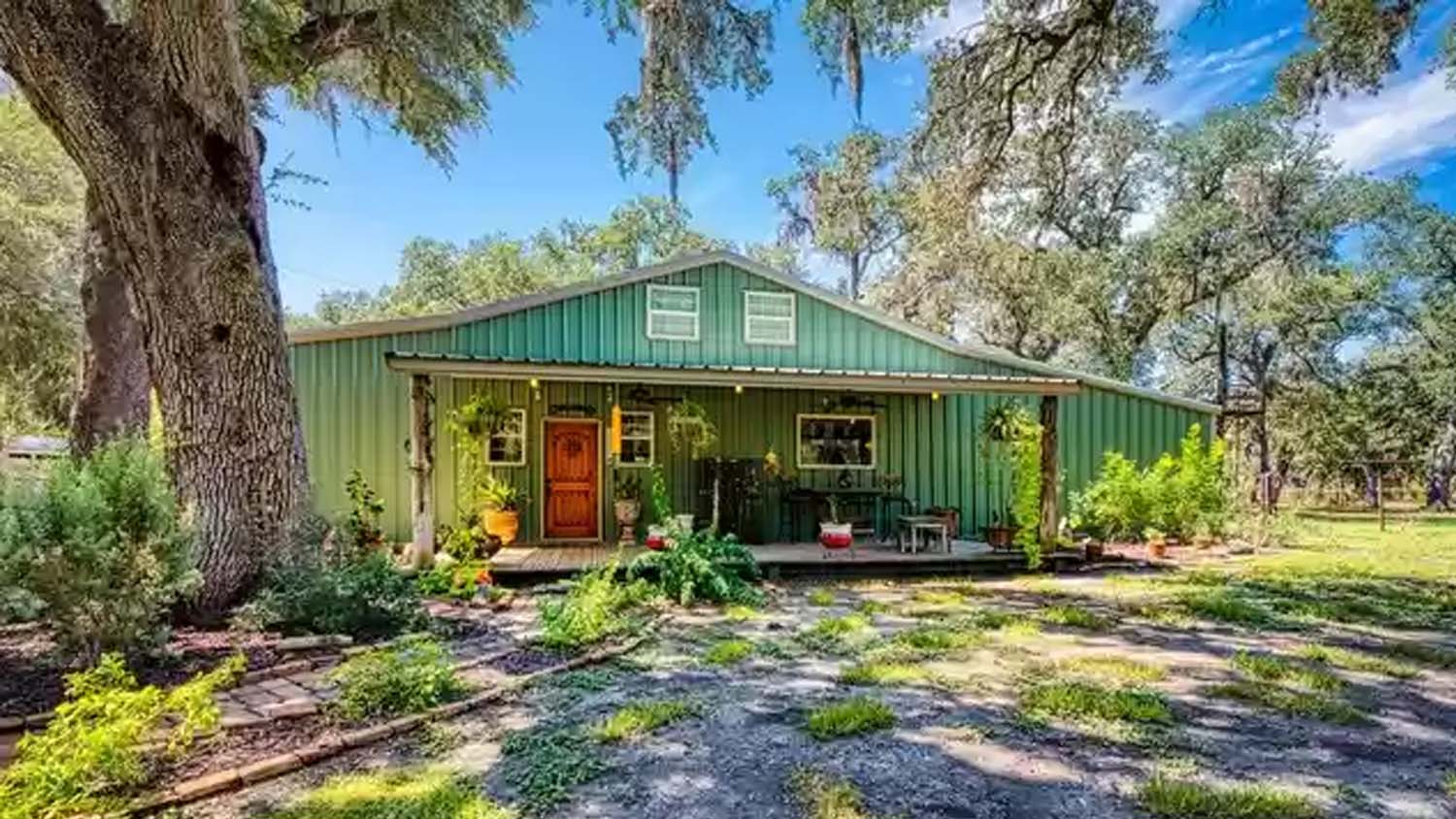 Green barn-like home with a red front door and porch.
