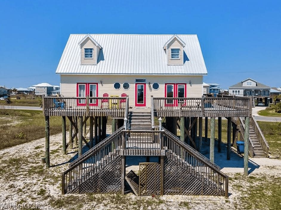 Back view of tan and red beach house with double staircase. 