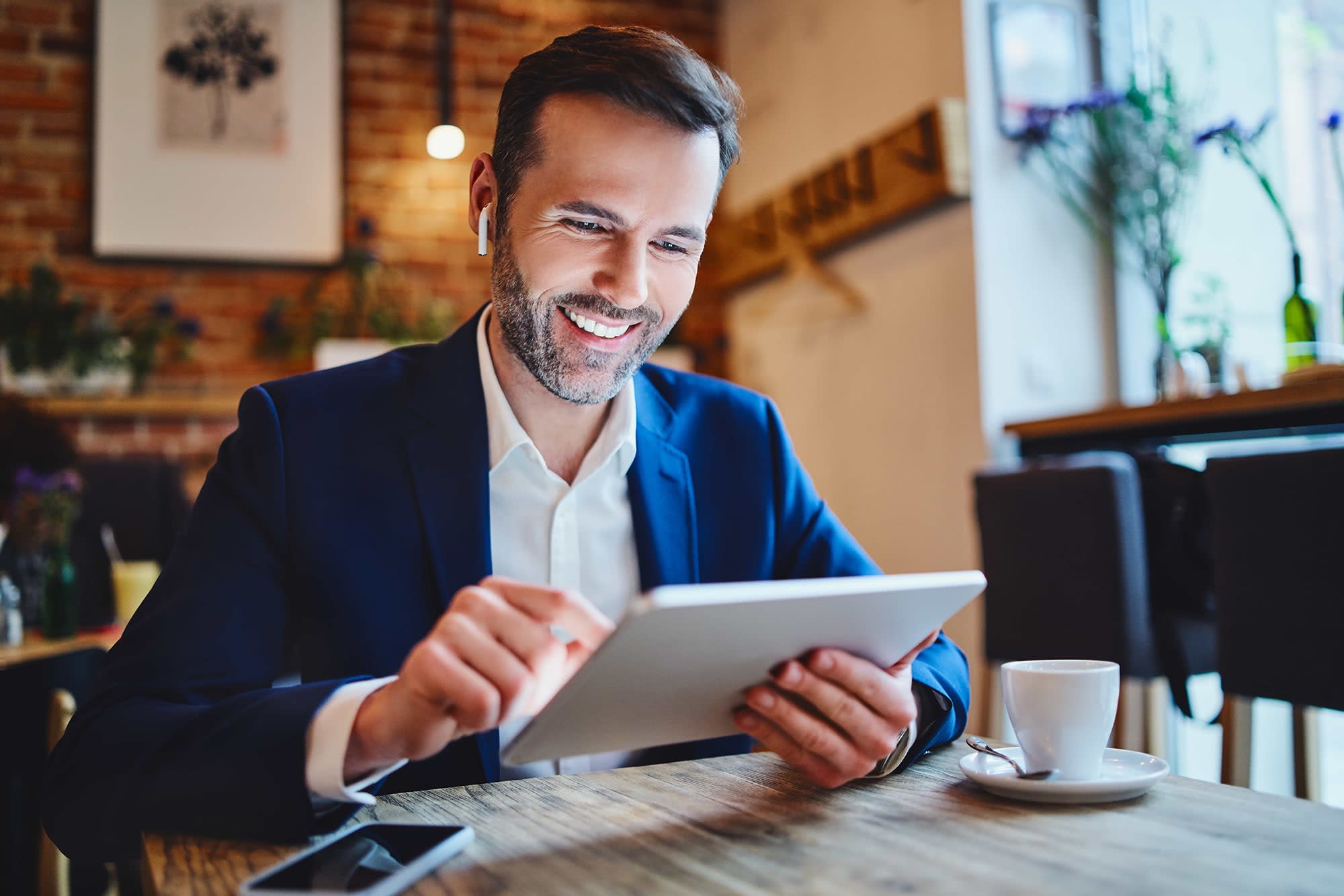 A man sitting in a coffee shop doing work on his Ipad. 