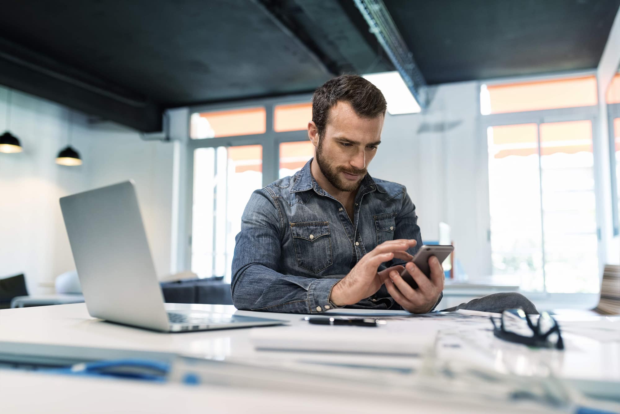 A man sitting at a desk scrolling on his phone. 