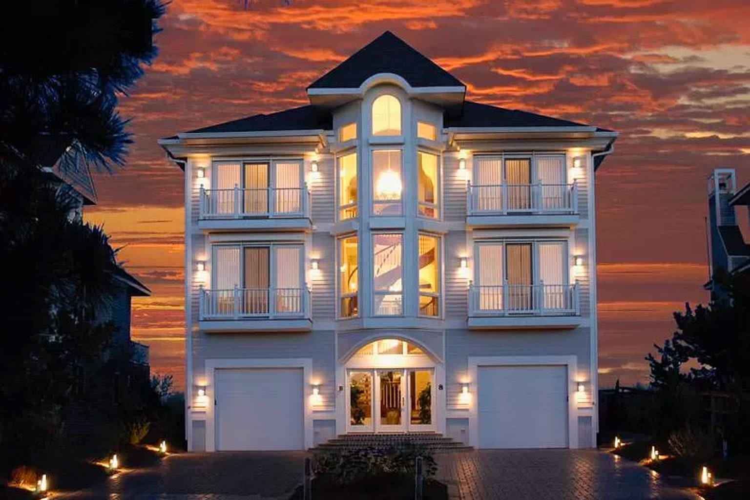 Two story white beach house, taken a night with a beautiful pink and orange sky. 