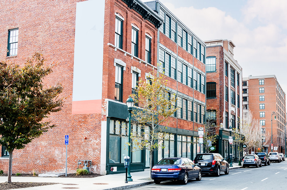Street view of brick buildings with cars parked on the road next to sidewalk.