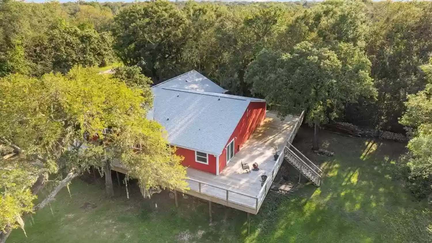 Aerial view of a red elevated house surrounded by a porch and stairs leading to the ground. 