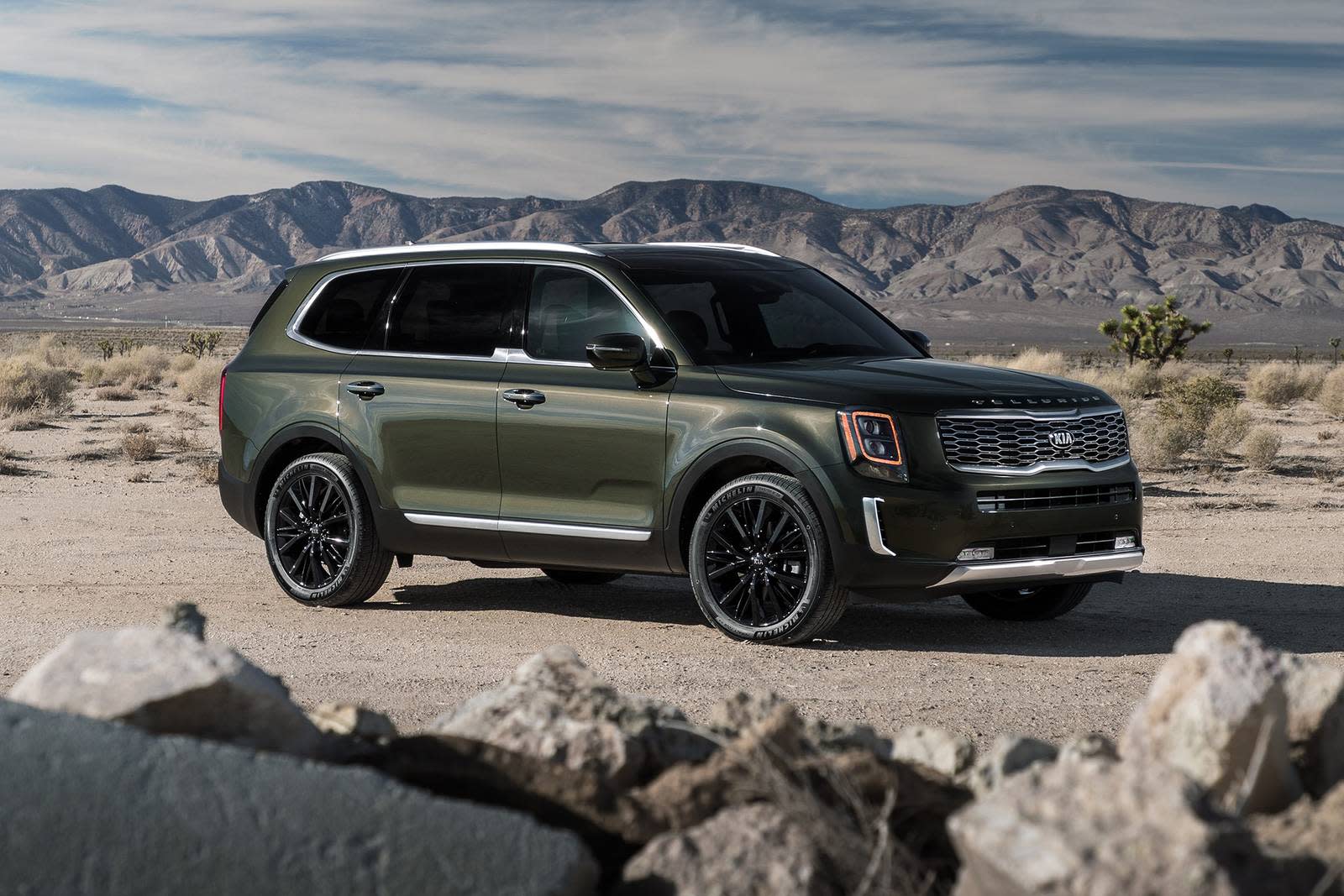 Green Kia Telluride in desert environment with mountains in background.
