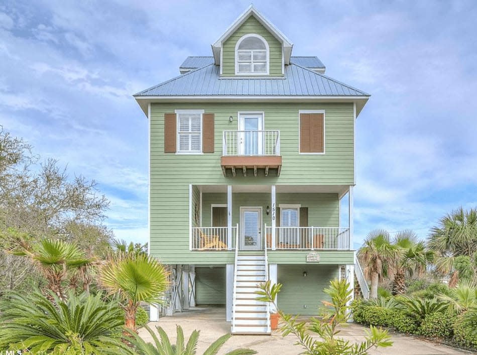 Outside view of green beach house with one single staircase. 