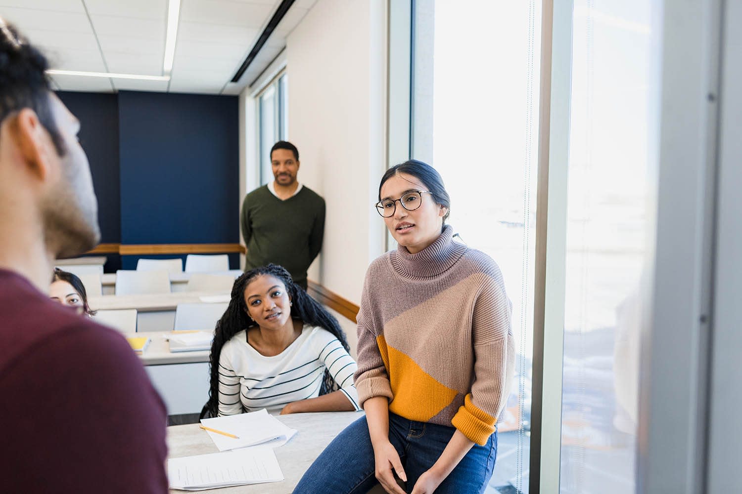 People sitting and standing in a classroom face a man who is speaking toward them.