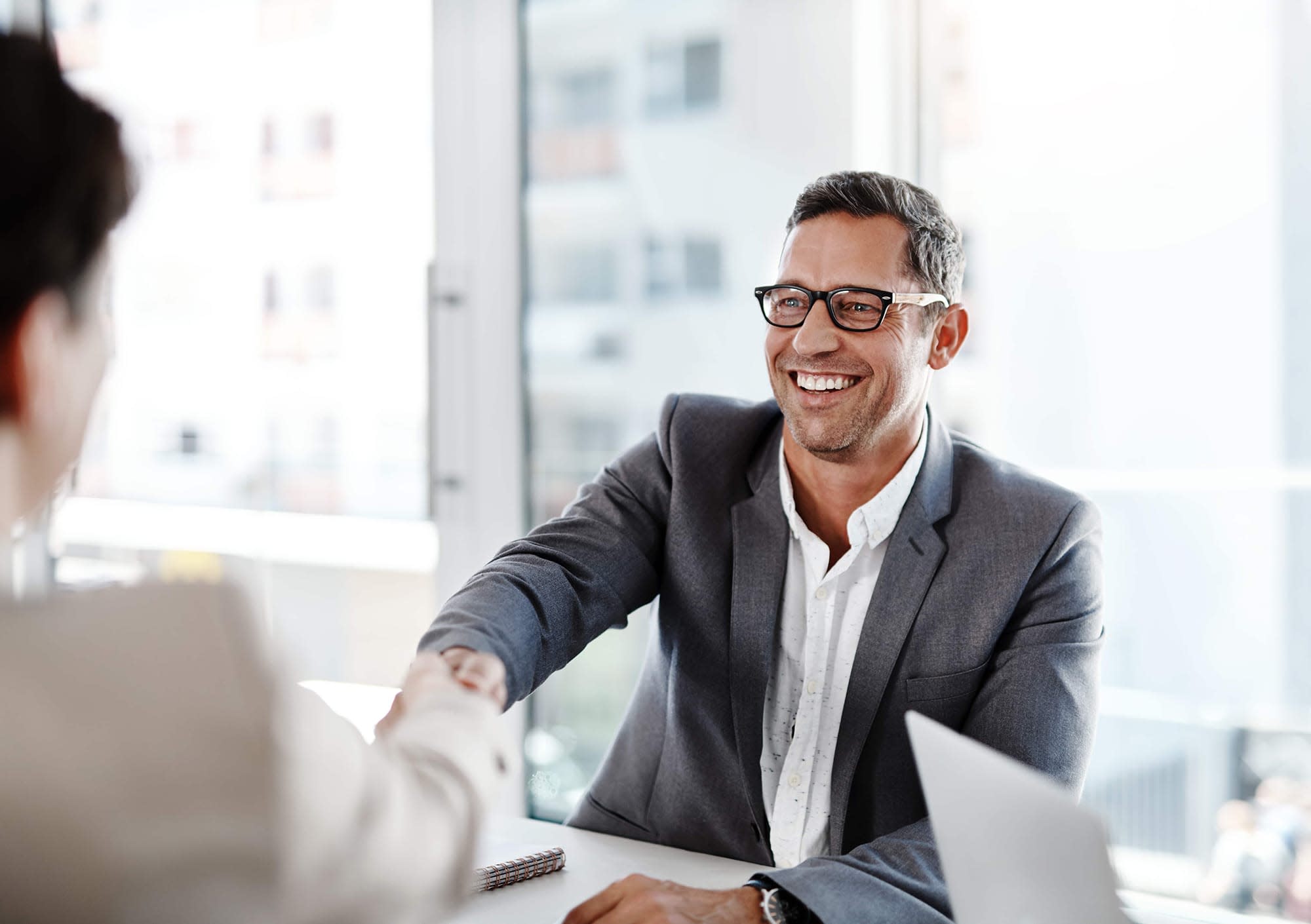 Man smiling at a person facing him while shaking their hand.