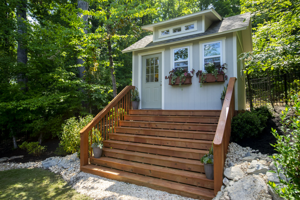 Small green house in a forest with wooden steps leading up to the house.