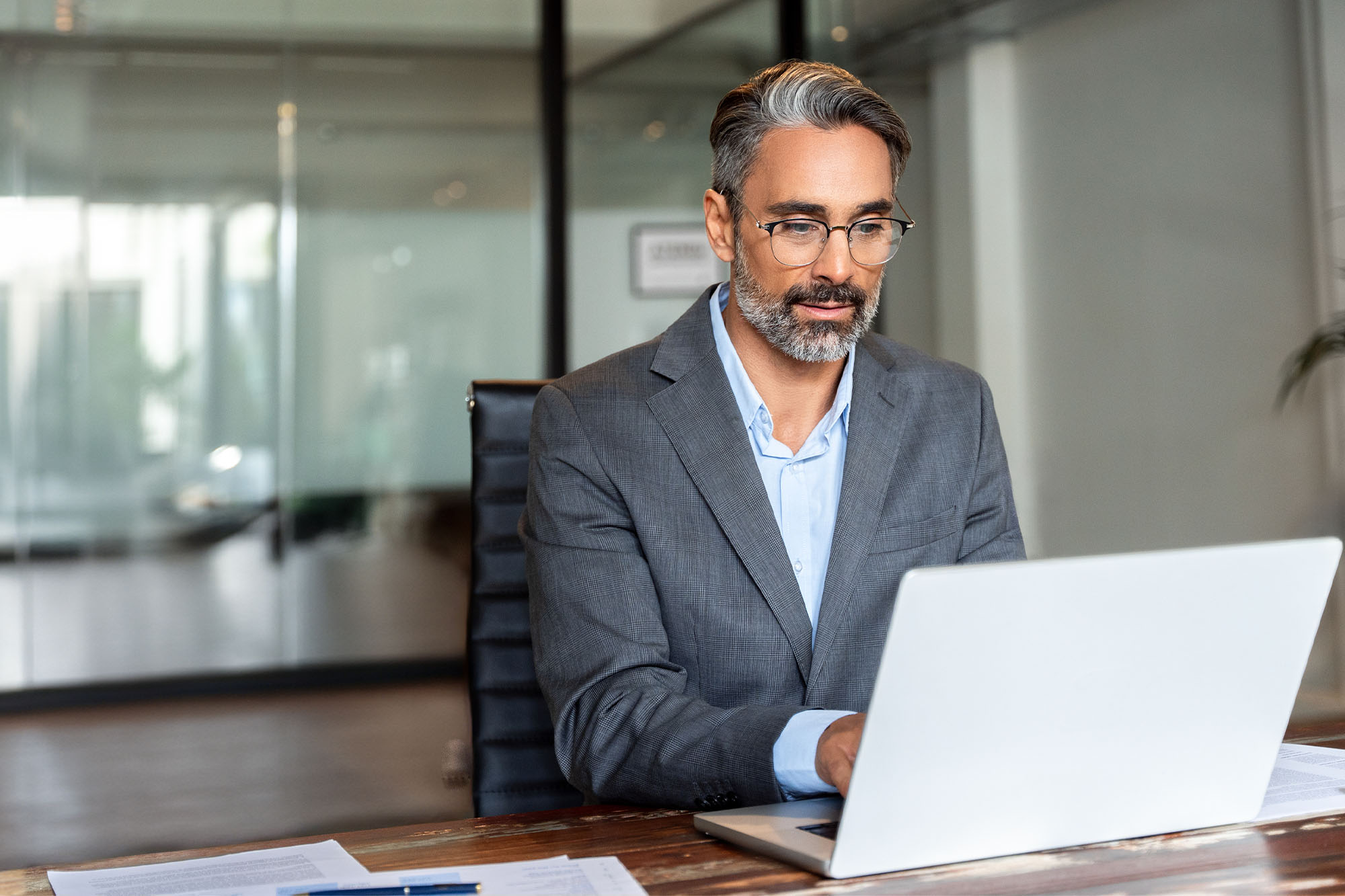 Mortgage loan officer working on a laptop in a modern office, wearing a suit and glasses.