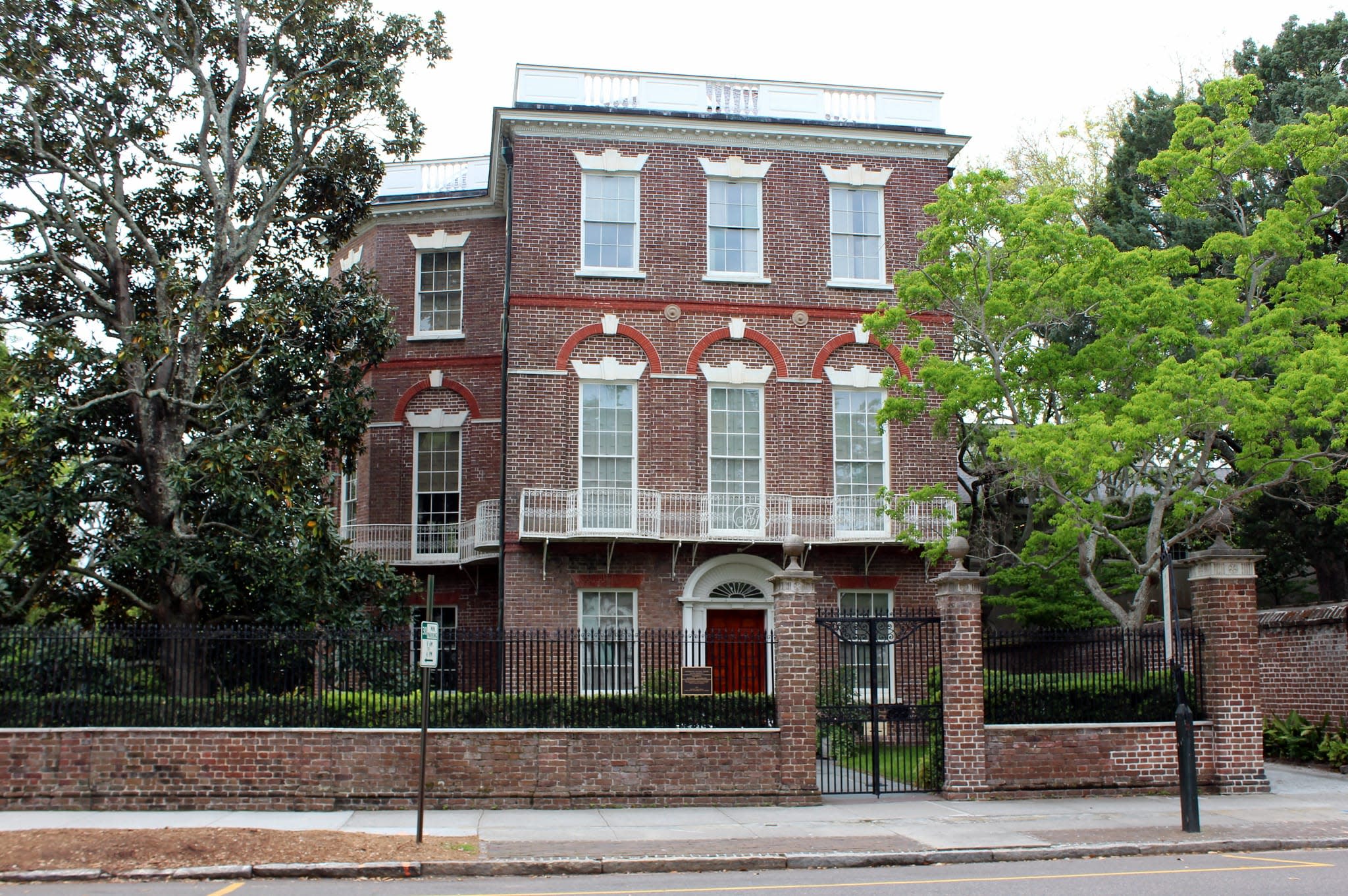 Three story Federalist style home behind a black gate.