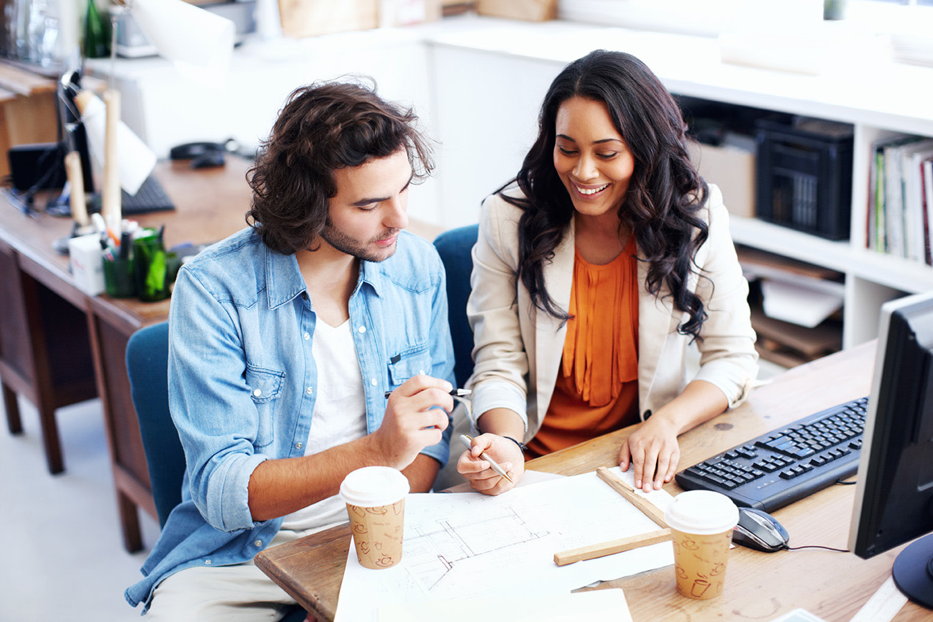 A woman and a man both with pens in their hands over a piece of paper. 