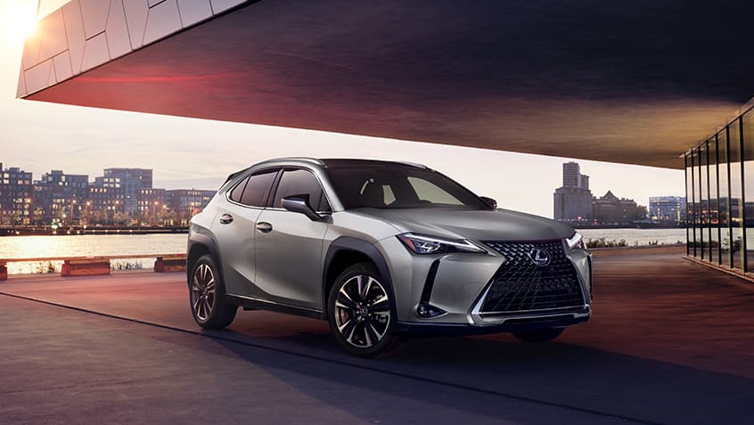 Silver Lexus UX 250h parked under a building cover with water and buildings in the background.