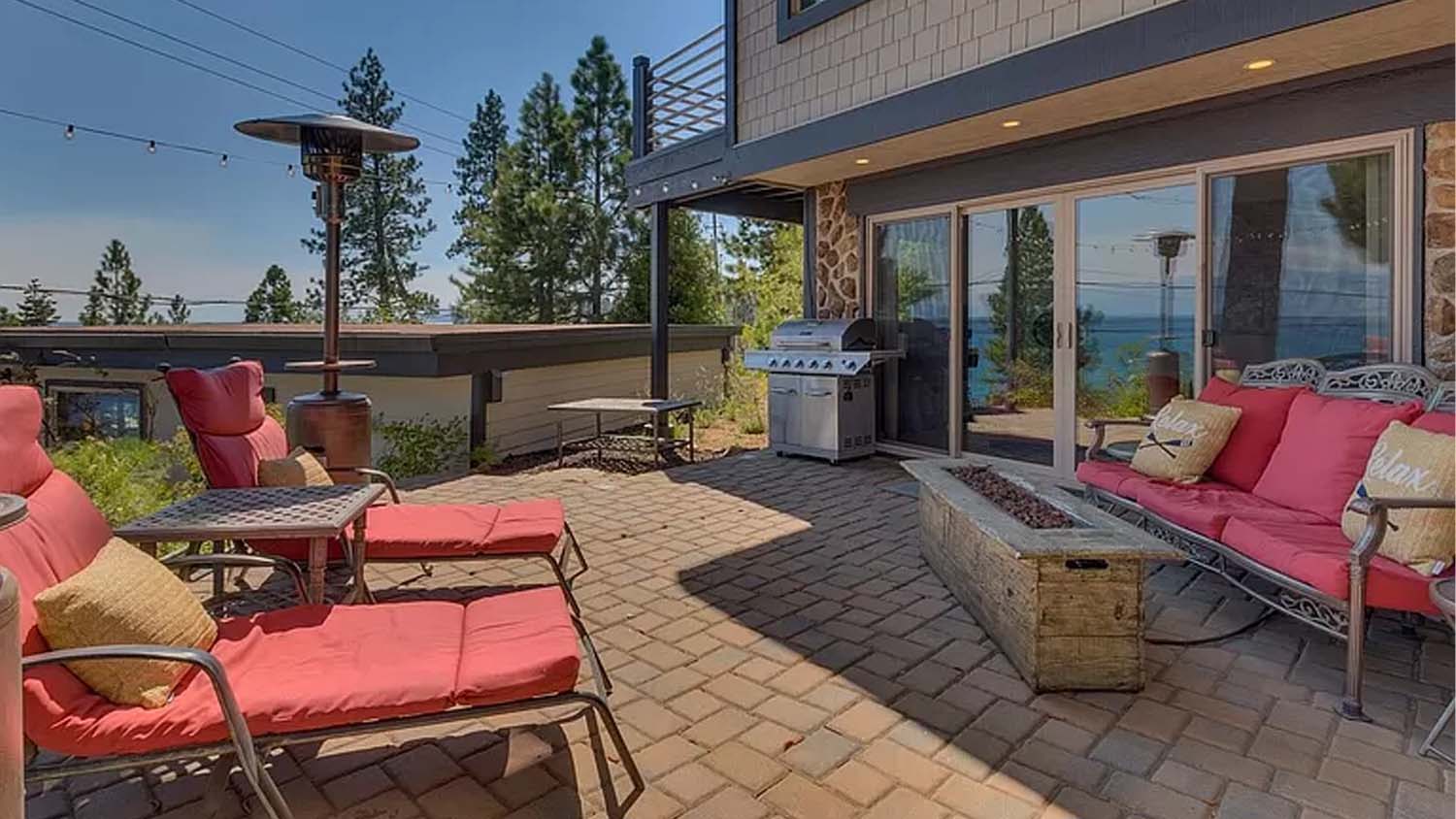 Back porch of home in Carnelian Bay with a red-cushioned couch and lounge chairs, fire pit, and grill.