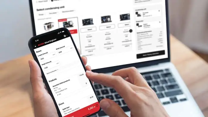Person holding smartphone showing shopping cart while laptop displays product comparison page in background