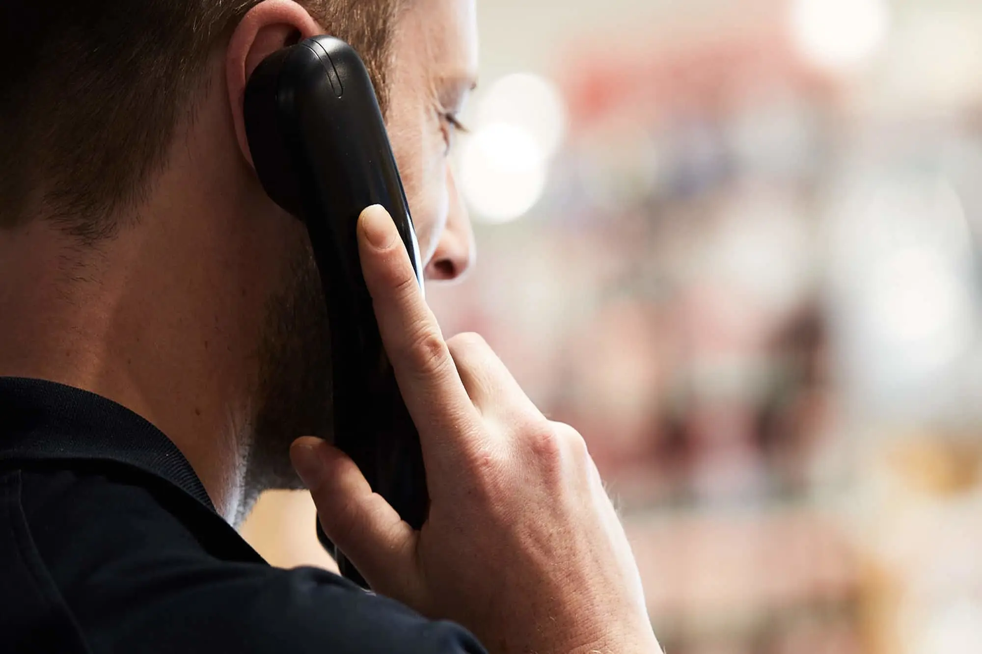 Person holding a black phone to their ear during a phone call with blurred background.