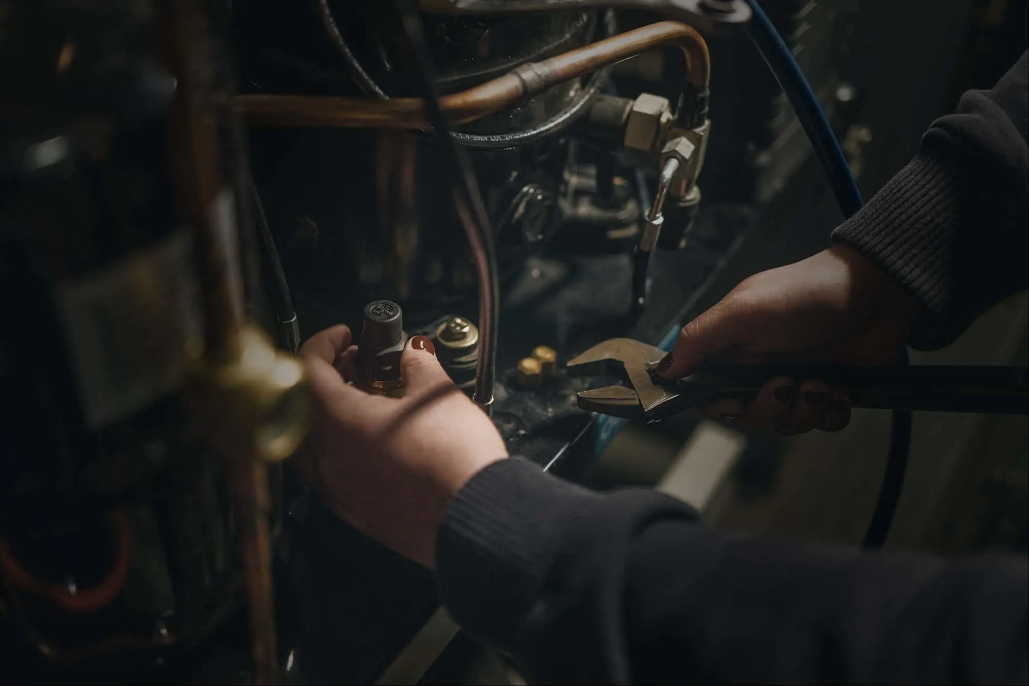 Hands holding a socket and wrench while working on copper pipes with metal components visible.