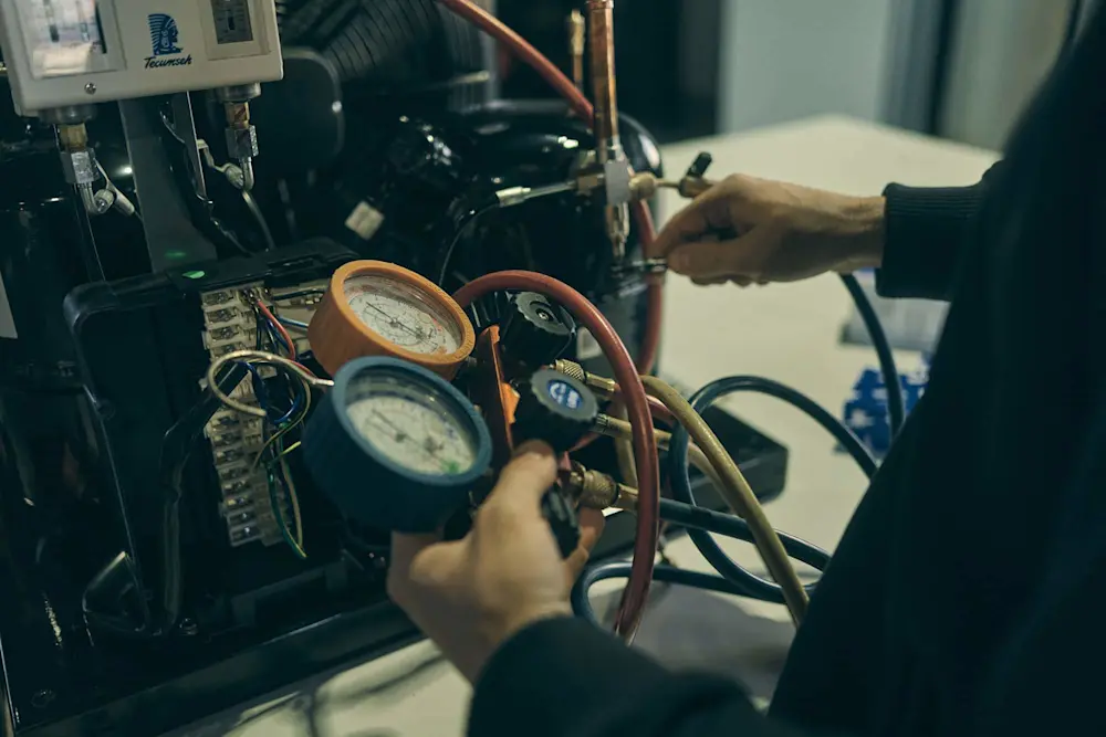 Technician holding pressure gauges with colored hoses while servicing HVAC equipment.