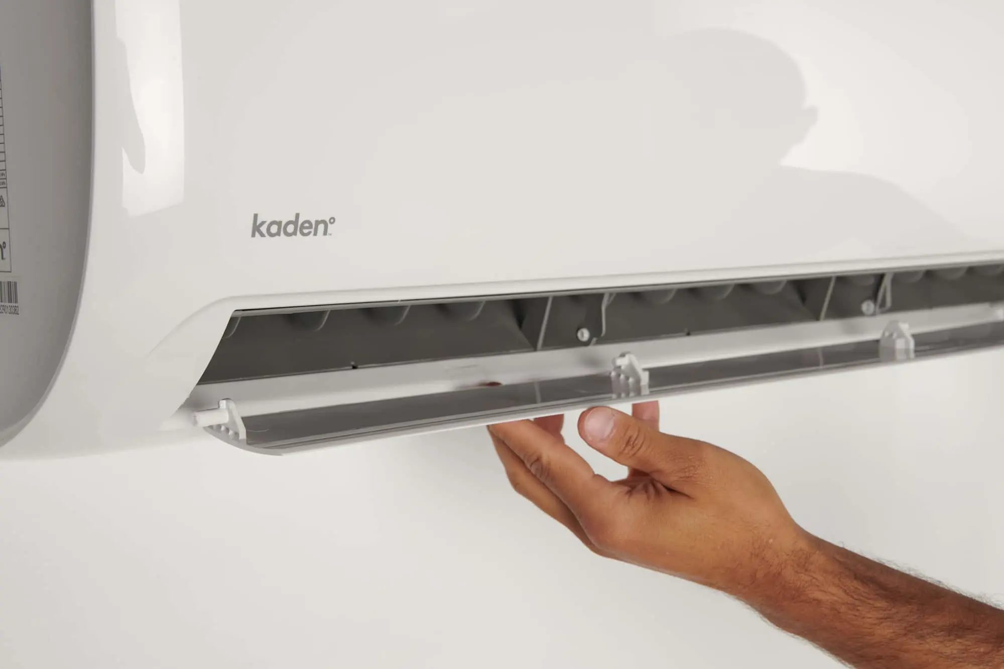 Hand opening the front panel of a white Kaden air conditioning unit mounted on a wall.