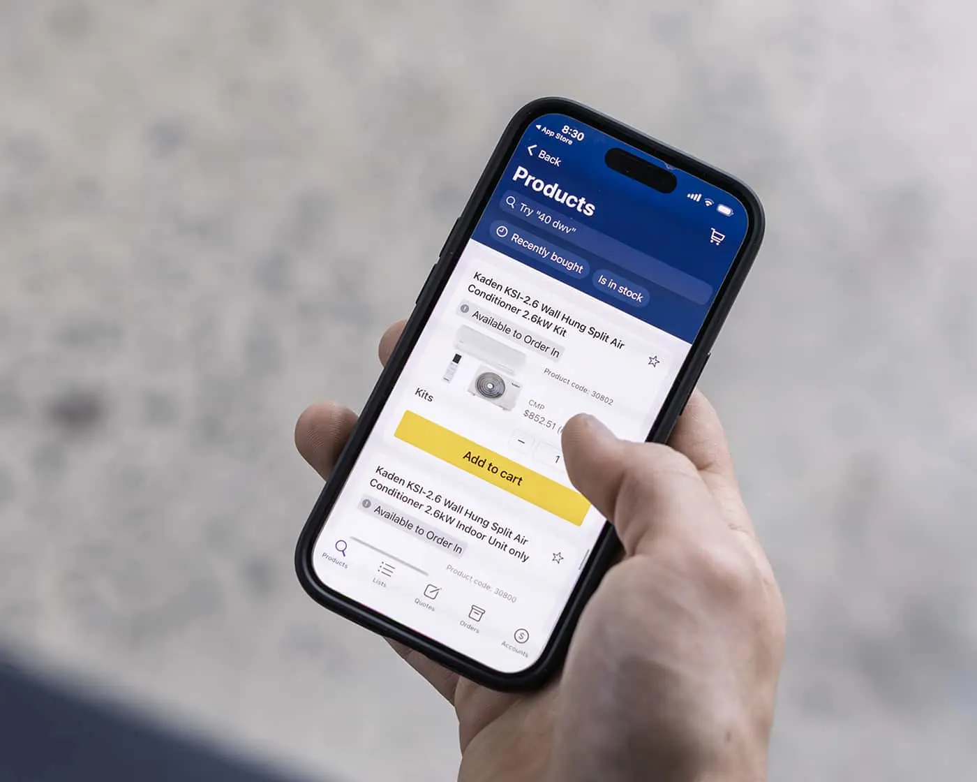 Hand holding smartphone displaying product page with air conditioner unit and yellow add to cart button.