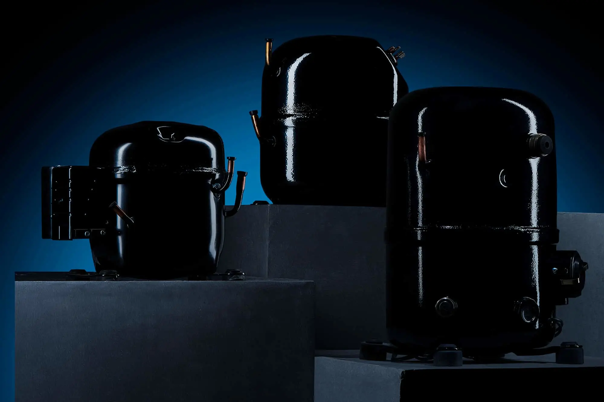 Three black cylindrical compressor units displayed on gray platforms against a dark blue background.