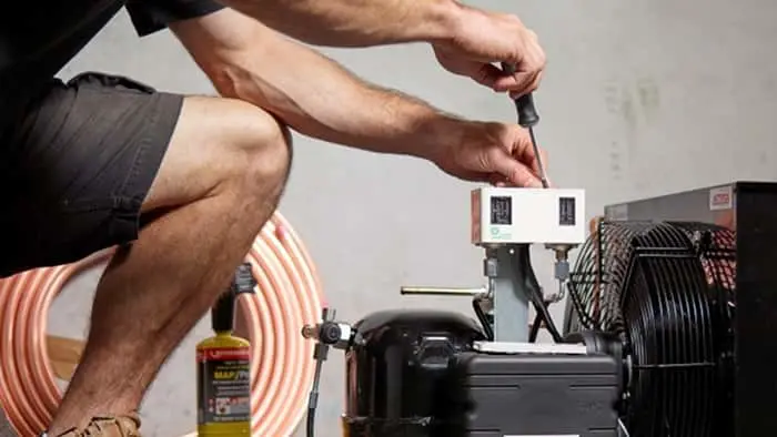 Person adjusting controls on an air compressor unit with coiled hose nearby