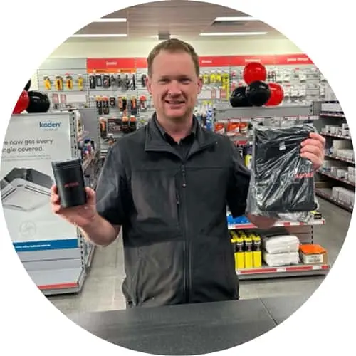 Man in dark shirt holding keep cup and packaged product in retail store.