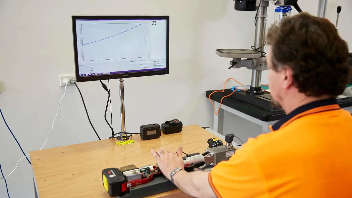 Person in orange shirt testing equipment while monitoring a graph on screen showing measurement data.
